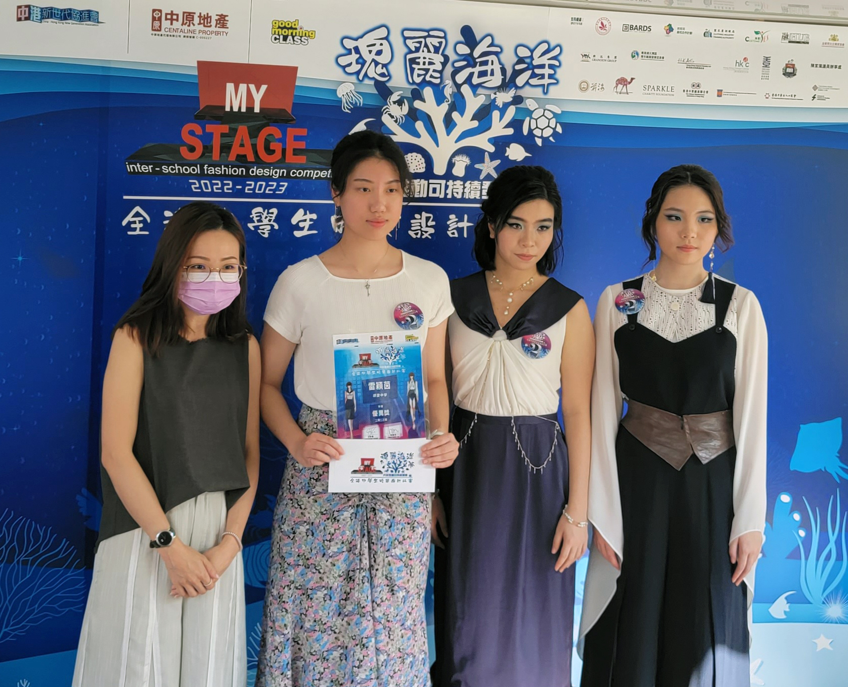 A group of women standing in front of a blue bannerDescription automatically generated